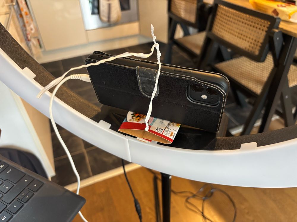 An iPhone strapped to a ring light via cable ties and M&S Salt and Pepper Chicken cardboard packaging