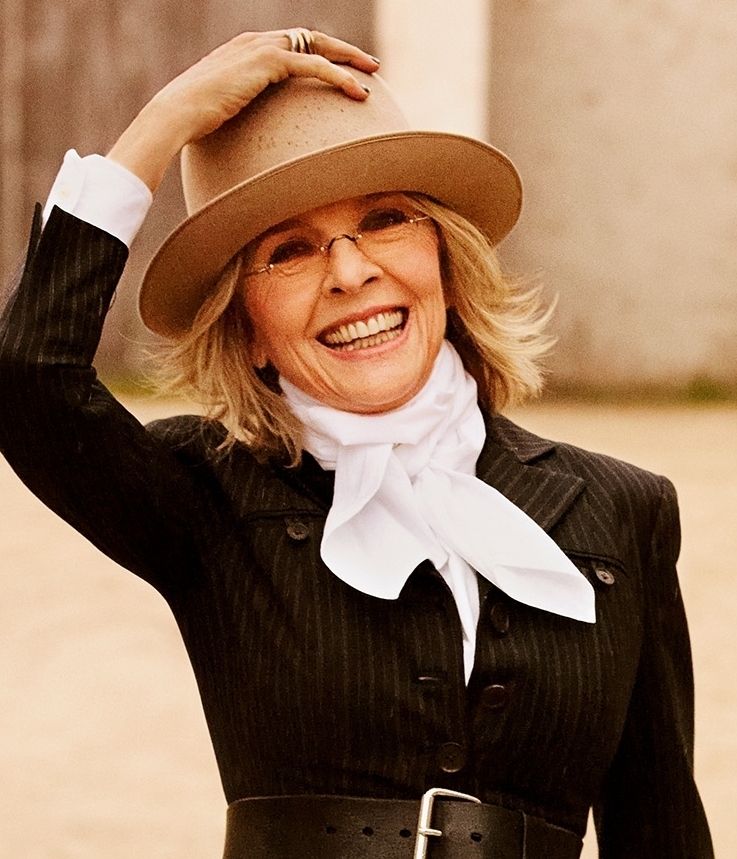 Diane Keaton in her signature outfit wearing a beige hat and a scarf