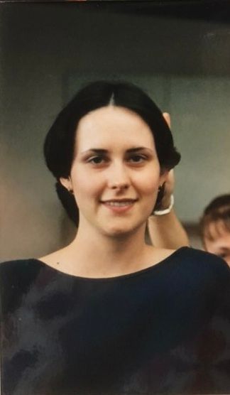 Photo of Elizabeth at 20 yrs old. She is wearing her hair in a bob, she has a black shirt on, and someone is holding two fingers up behind her.