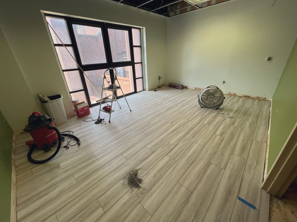 An in-progress room with lvp flooring laid down. The walls are green/white and there's a huge window overlooking a courtyard area. Not pictured: Spinch is tired