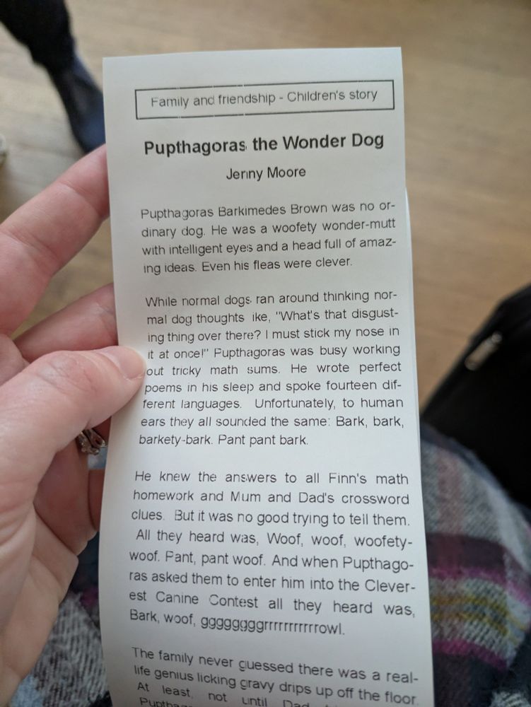 The start of a short story on a long scroll (like a long receipt). The sorry is Pupthagoras the Wonder Dog by Jenny Moore. The visible text reads,

Pupthagoras Barkemedes Brown was no ordinary dog. He was a woofety wonder-mutt with intelligent eyes and a head full of amazing ideas. Even his fleas were clever.

While normal dogs ran around thinking normal dog thoughts like "What's that disgusting thing over there? I must stick my nose in it at once!" Pupthagoras was busy working out tricky math sums. He wrote perfect poems in his sleep and spoke fourteen different languages. Unfortunately, to human ears they all sounded the same: Bark, bark, barkety-bark. Pant pant bark.

He knew the answers to all Finn's math homework and Mum and Dad's crossword clues. But it was no good trying to tell them. All they heard was, Woof, woof, woofety-woof. Pant pant woof. And when Pupthagoras asked them to enter him into the Cleverest Canine Contest, all they heard was, Bark, woof, gggggggrrrrrrrrrrrooooowl.

The family never guessed there was a real life genius licking gravy drips up off the floor...