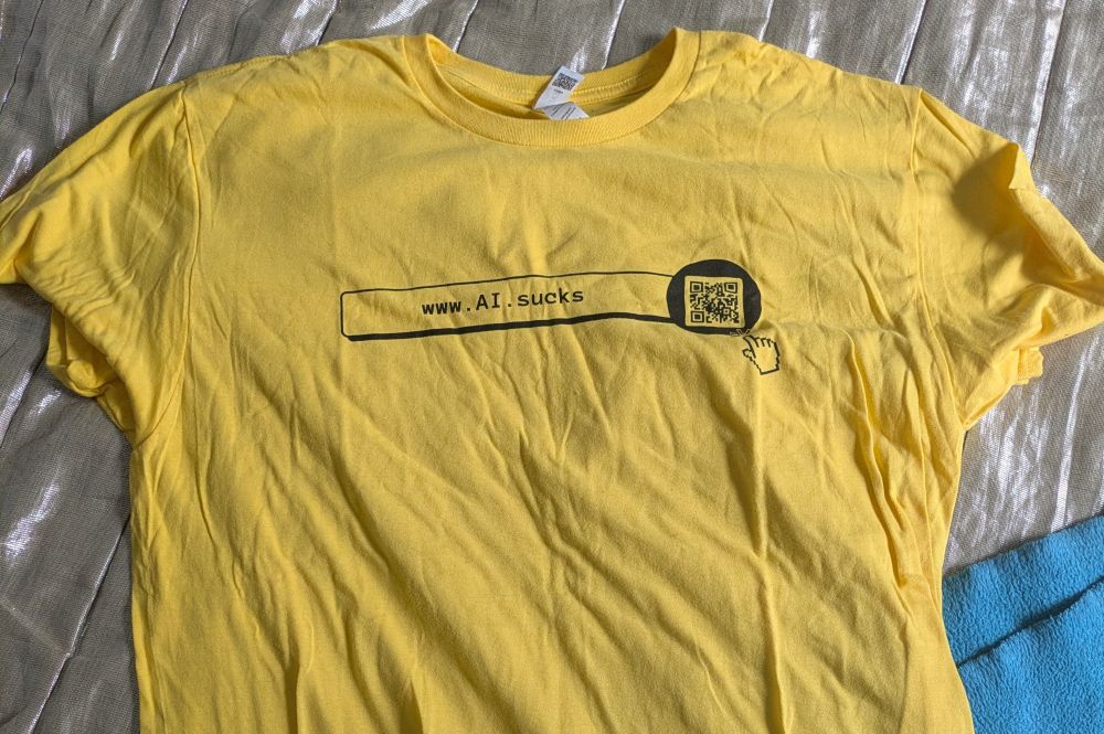 A very yellow t-shirt with a text box and a QR code on it. The text in the text box is a URL: www.AI.sucks