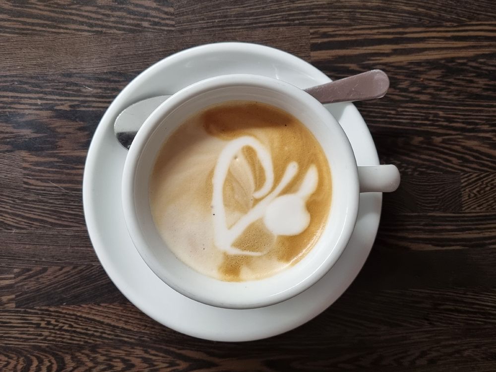 Cappuccinotasse von oben fotografiert mit einem Muster im Milchschaum das aussieht wie eine Hieroglyphe. 