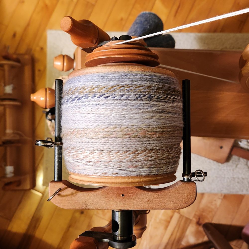 A jumbo bobbin on a spinning wheel is filled to capacity with a 2-ply yarn.