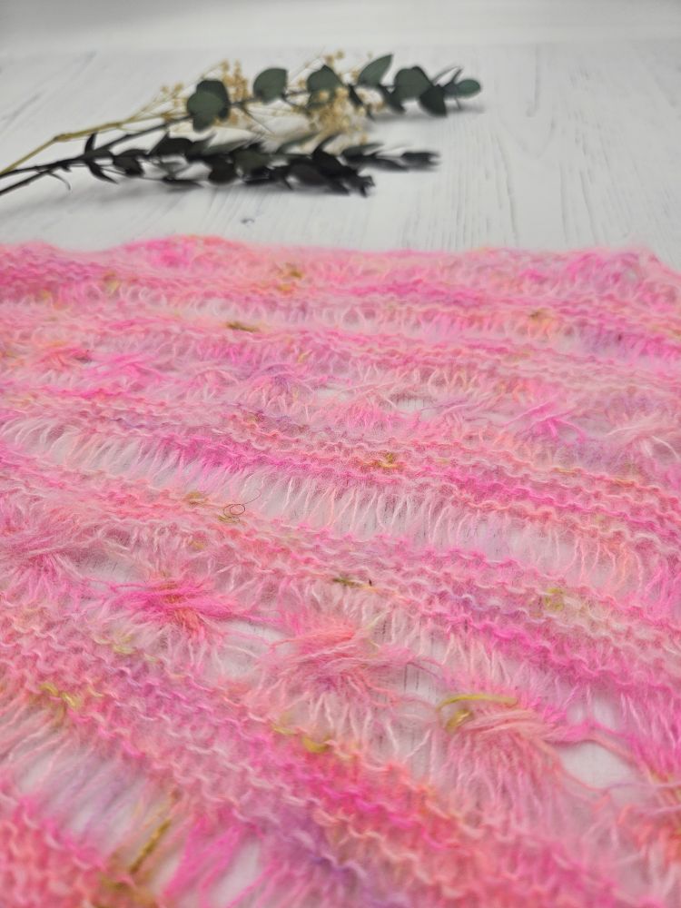 A close up of a lacy stitch pattern in bright pink fluffy laceweight yarn