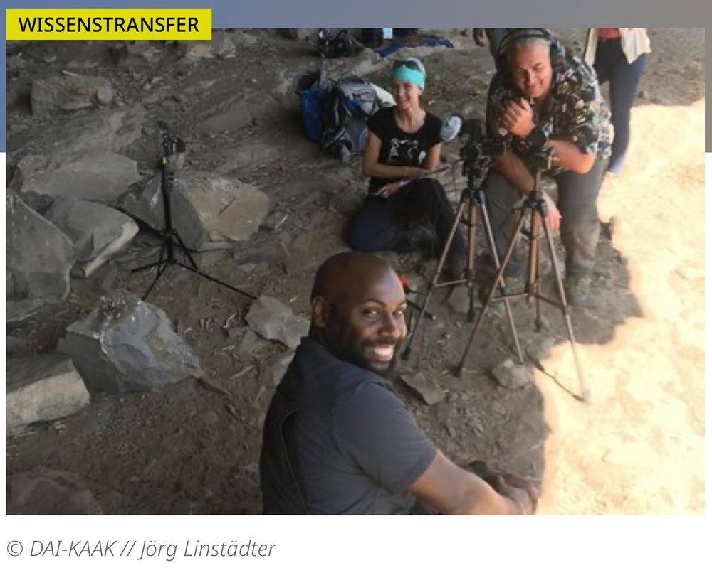 Screenshot, der mehrere Personen mit Filmausrüstung im Gelände zeigt.