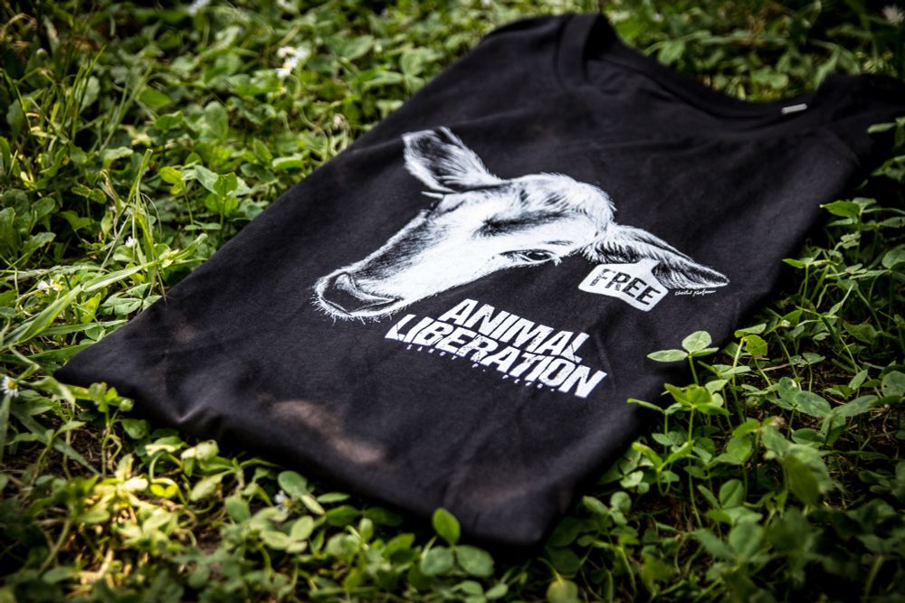 T-Shirt mit Statement im Gras. Das Motiv zeigt den Kopf von einem Kalb und das Statement: Animal Liberation. 
