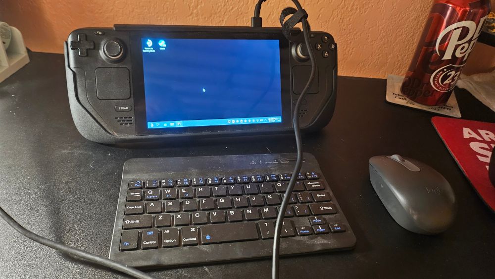 A steam deck propped up on a desk with a small keyboard and mouse. 
