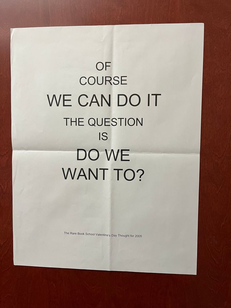 Reddish wood door with slightly creased white paper poster. Black all-caps lettering reads “Of course we can do it the question is do we want to?” Small black lettering below identifies this as The Rare Book School Valentine’s Day Thought for 2005. 