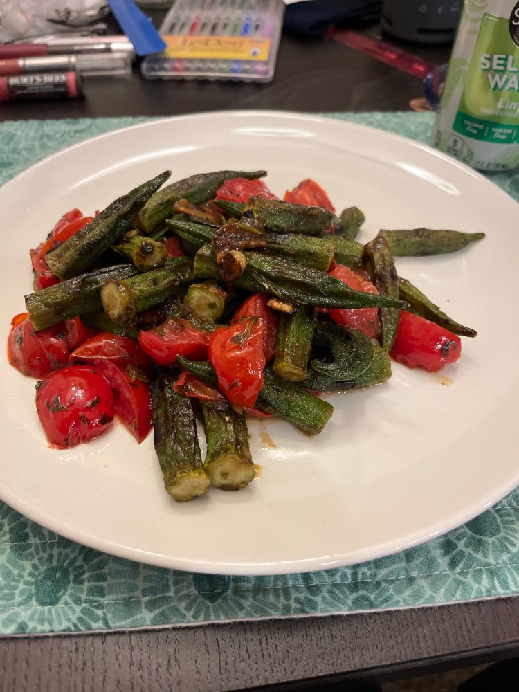 White plate on a teal mosaic-pattern placemat. The plate has a large serving of a tomato and okra dish. 
