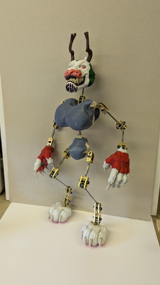 A puppet/character doll of a white and red lion with branch like horns. It's just the metal armature and grey coring that is visible.