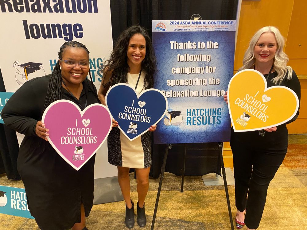 Our team holding heart-shaped boards that say "I love school counselor," standing by a sign showing that we sponsored the conference relaxation lounge.