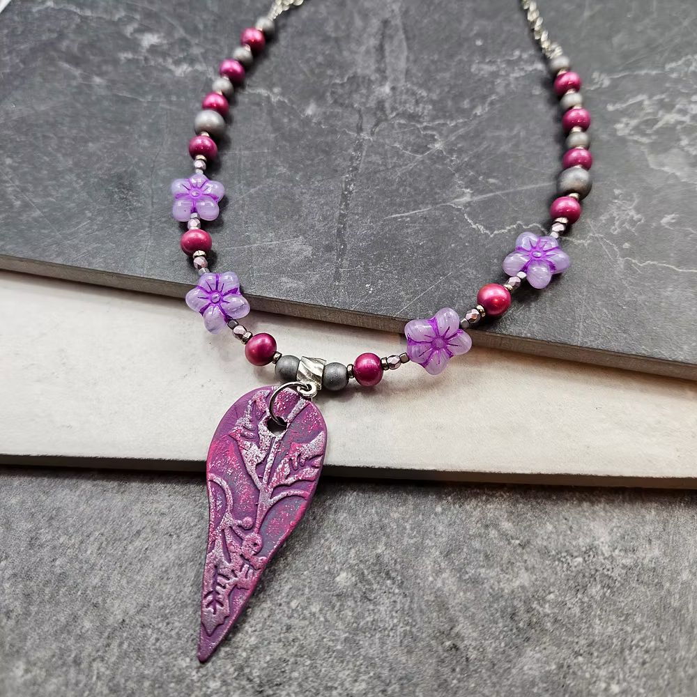 A stunning pink floral handmade ceramic pendant strung with pink and light purple beads.
