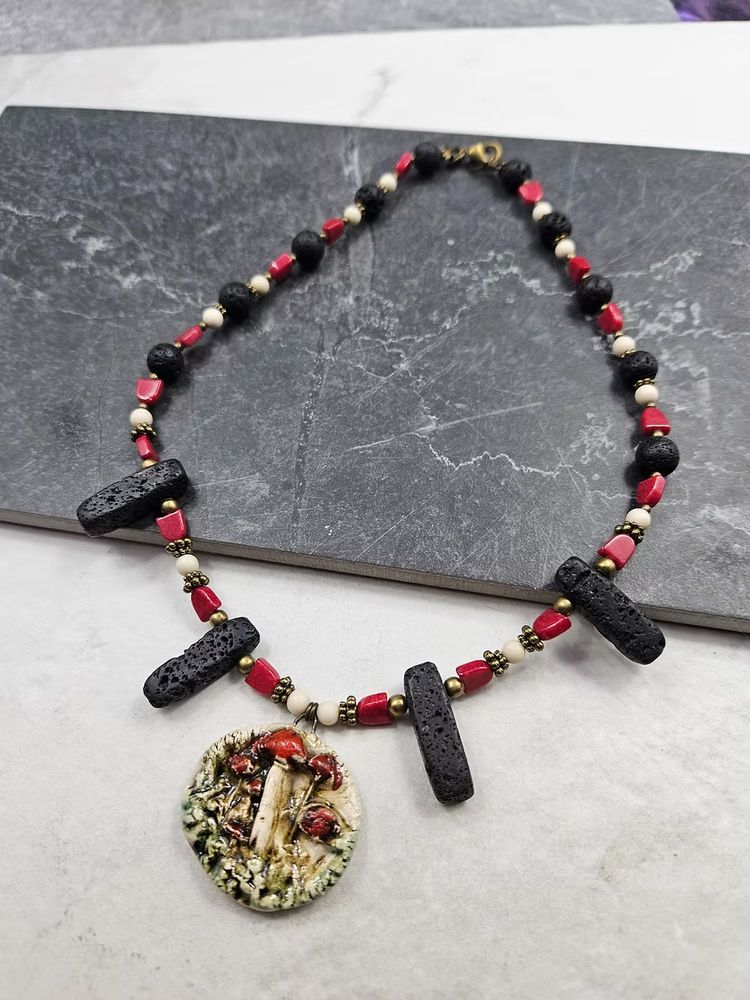 A rustic woodland ceramic focal with bright red and white mushrooms, strung on a necklace of red, white, and blocky black beads