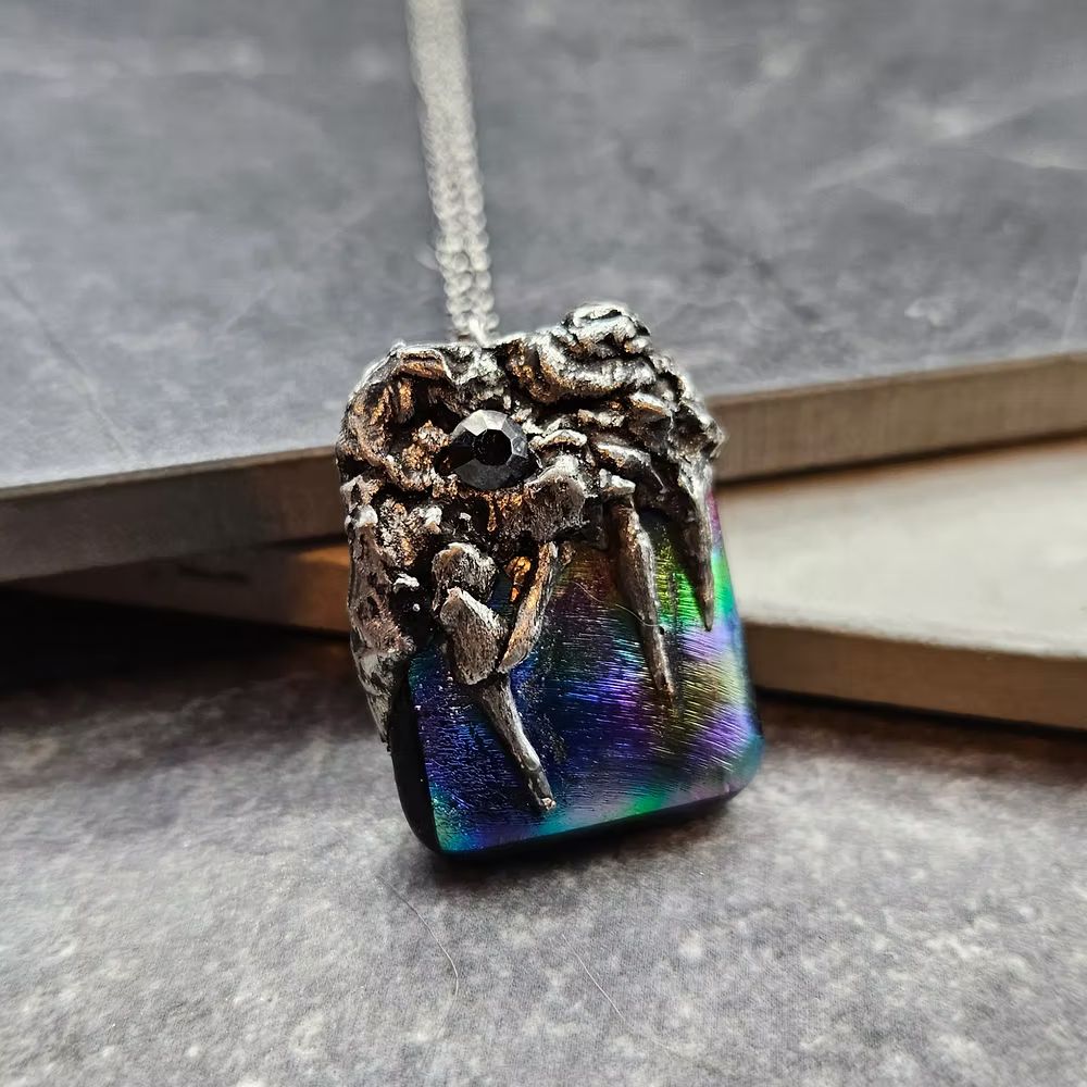 A gorgeous, iridescent rectangle of rainbow dichroic artisanal glass, clutched by hand-soldered rugged claws and strung on a chain.