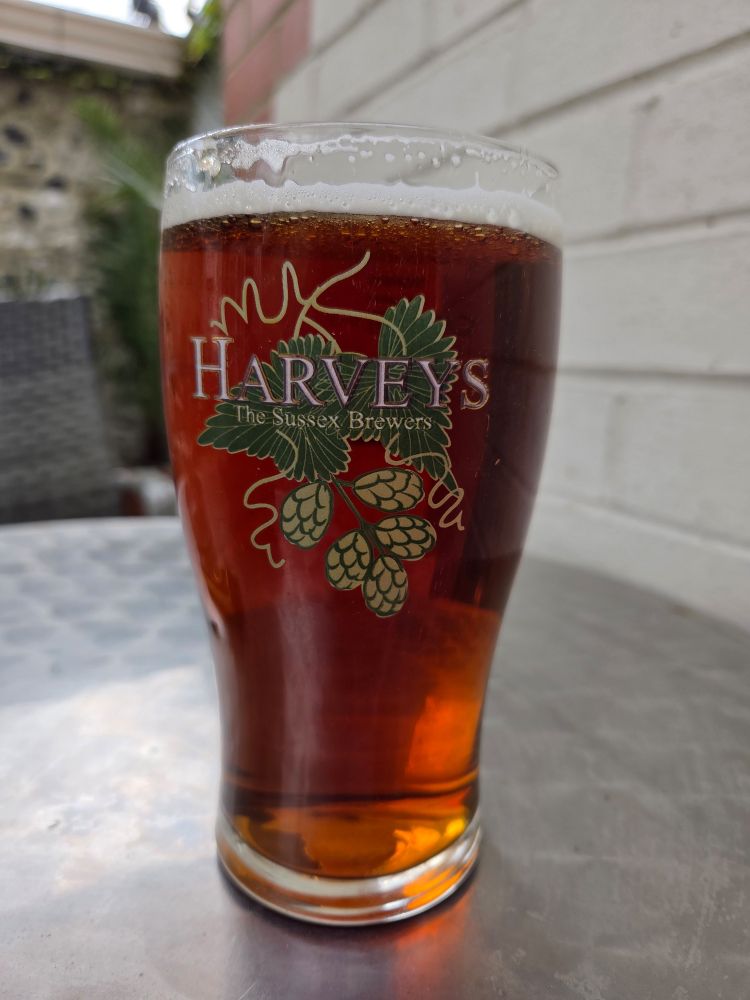 A pint of Harveys Best Bitter, less one sip, in a Harveys glass sits on a metal table.