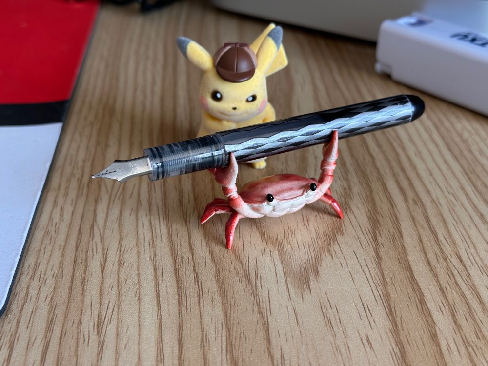 A plastic crab holds up an uncapped fountain pen while Detective Pikachu looks on from the back.