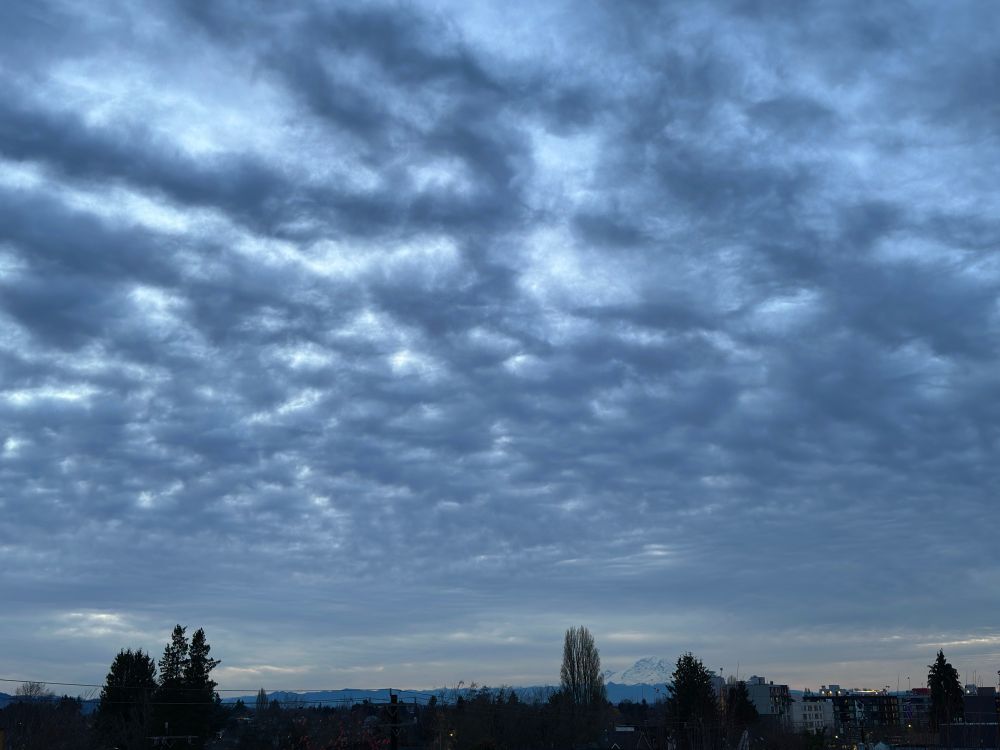 Light barely piercing grey clouds above My Rainier in distance