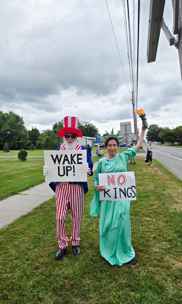 Uncle Sam with a sign saying "WAKE UP!" and Lady Liberty with a sign saying "NO KINGS"