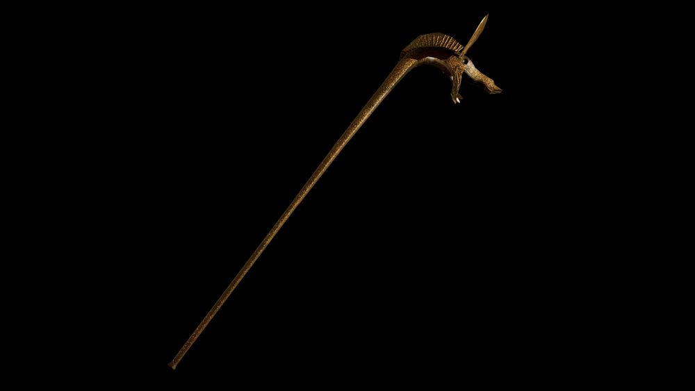 A full view of a 3D model of a carnyx. It has the visage of a boar, with an open, fanged mouth, a mane, and long, flat ears. It has a long tunnel to the mouthpiece. It is a metallic bronze, with evidence of time's wear.