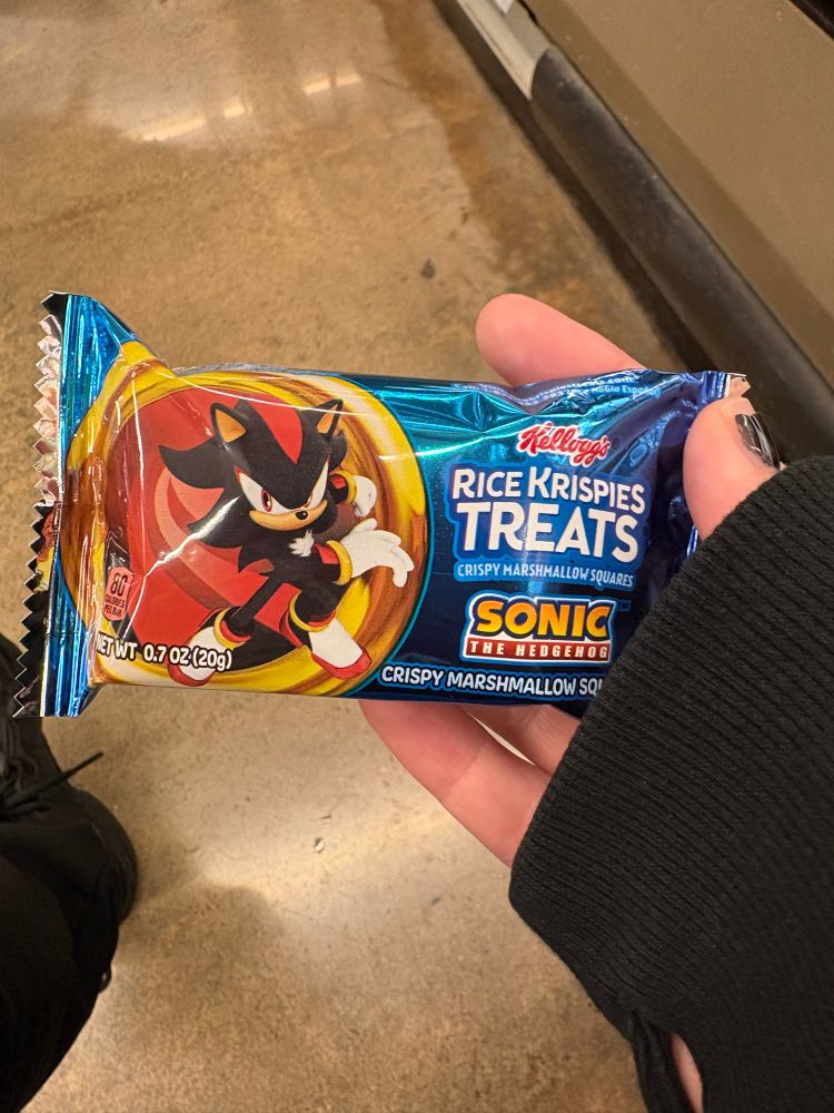 an emo looking(black nails, sweater paws) hand holding an individually wrapped Rice Crispy Treat with Shadow the Hedgehog on the wrapper