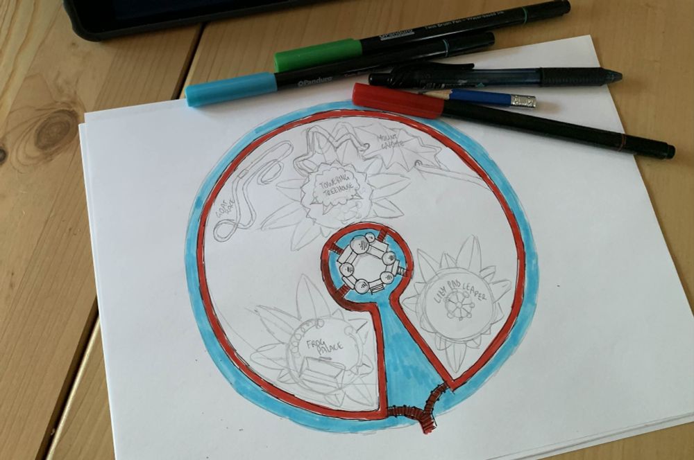 A pen and pencil sketch of a theme park map. The park is shaped like a huge lily pad, with a canal going around it and into the center wedge. Sketched out attractions include "the Goat Race", the "Towering Tree-House", "Mount Gnome", "Lily Pad Leaper" and the "Frog Palace".