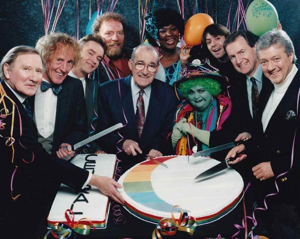 A panoply of celebs cutting a cake shaped like the Central TV logo.