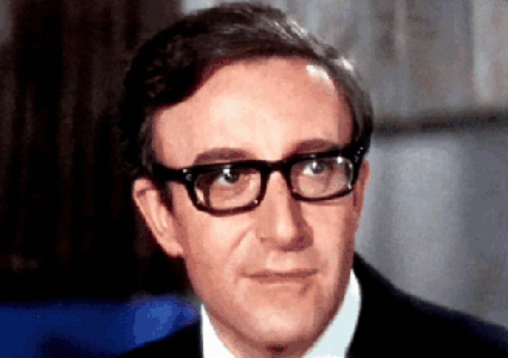 a man wearing glasses and a suit looks at the camera .