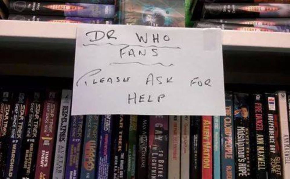 A sign taped to a shelf of books which says:

DR WHO FANS
PLEASE ASK FOR HELP

I heartily endorse this message.