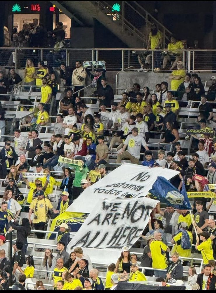 Attendees in the stands at a Nashville Soccer Club game holding a sign that reads “We are not all here.”