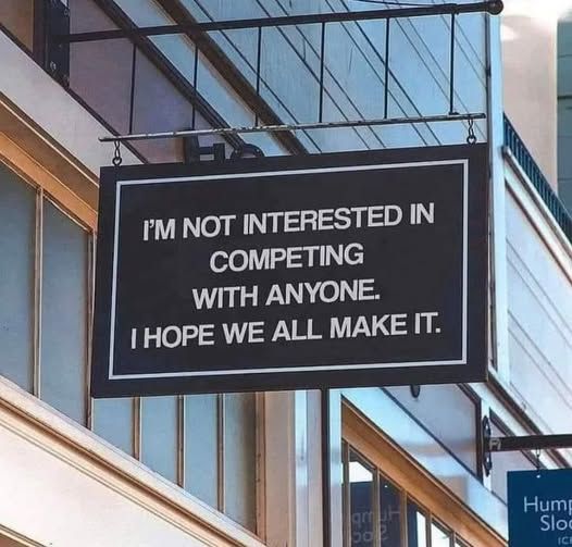 A black sign with white text that reads "I'm not interested in competing with anyone. I hope we all make it." 