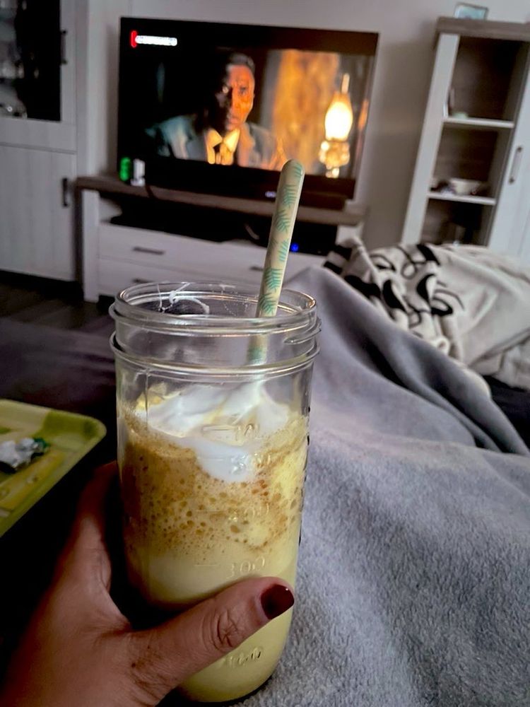 Liege eingekuschelt auf dem Sofa mit einem Becher goldene Milch in der Hand und schaue Serie