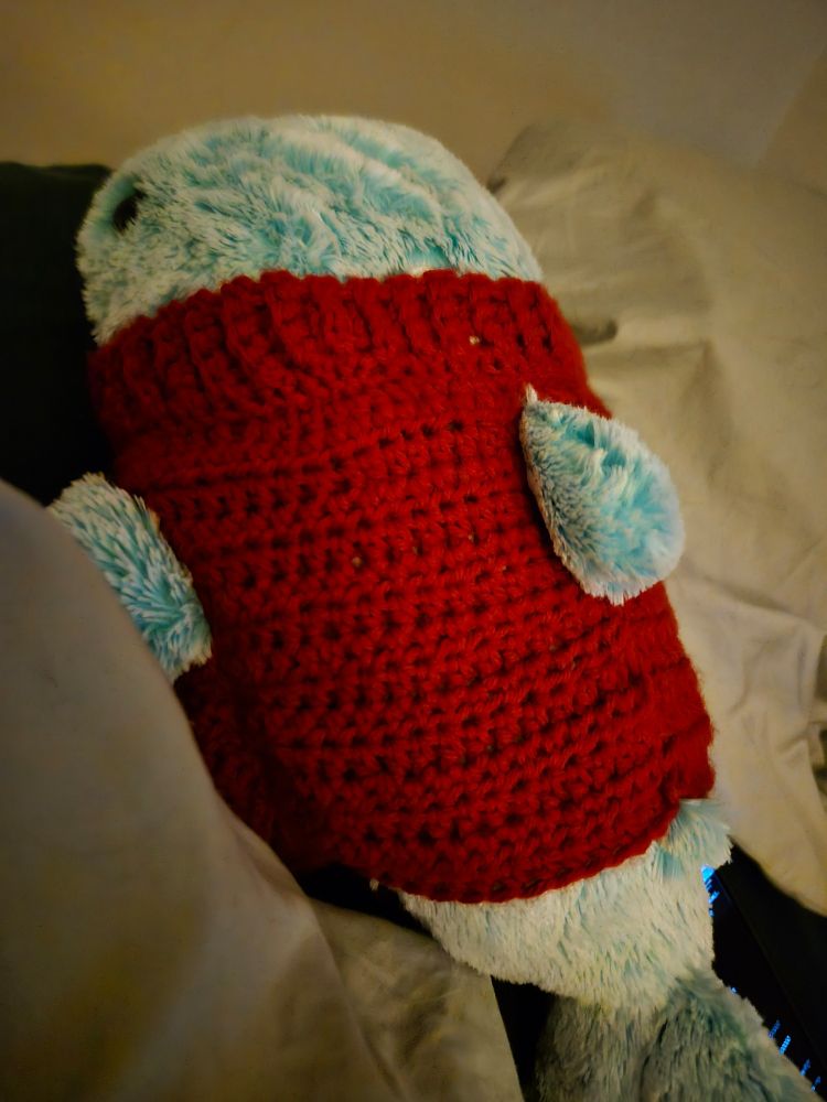 A Blue Whale stuffed animal wearing a red hand made crochet sweater.