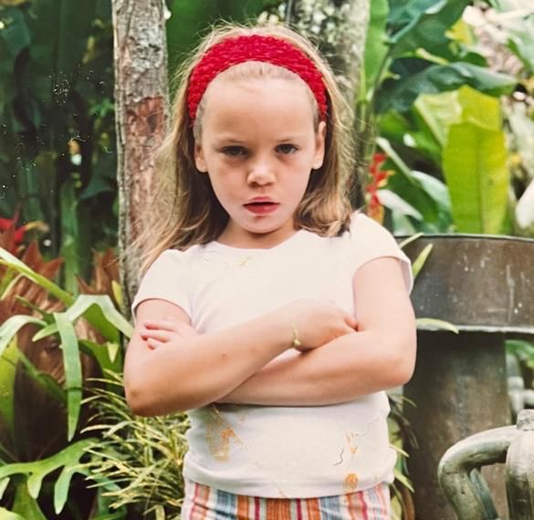 Criança loira de uns 7 anos emburrada, bem braba, com os braços cruzados