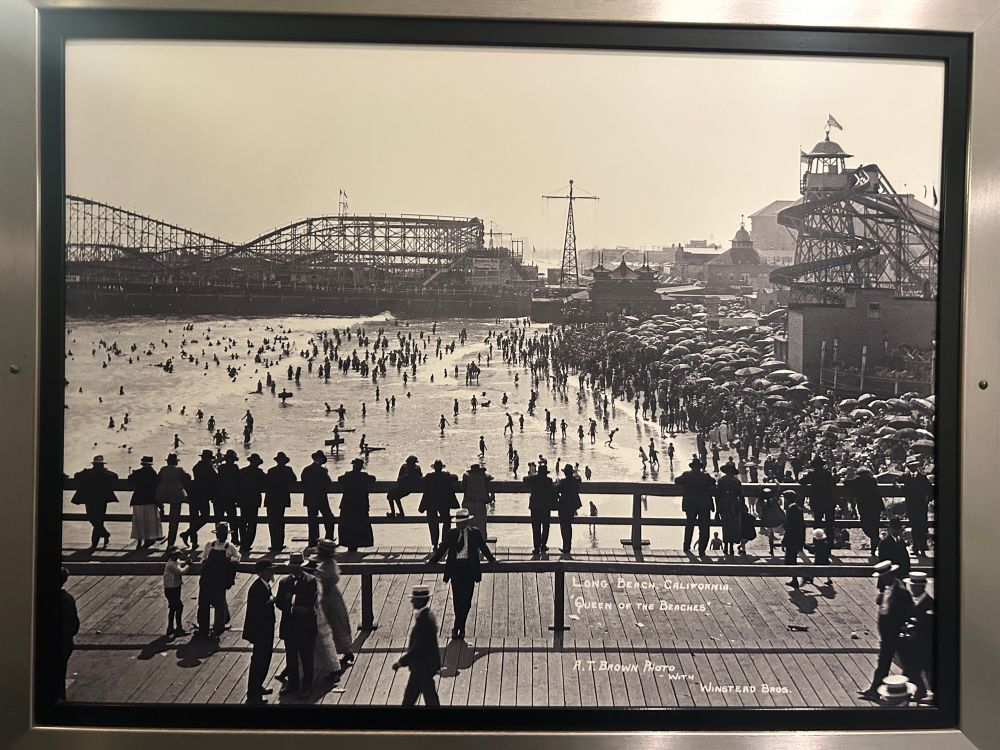 Photo of pier and beach, including roller coasters. Folks on beach are in wool suits and long dresses. The beach is absolutely packed with beach umbrellas. 