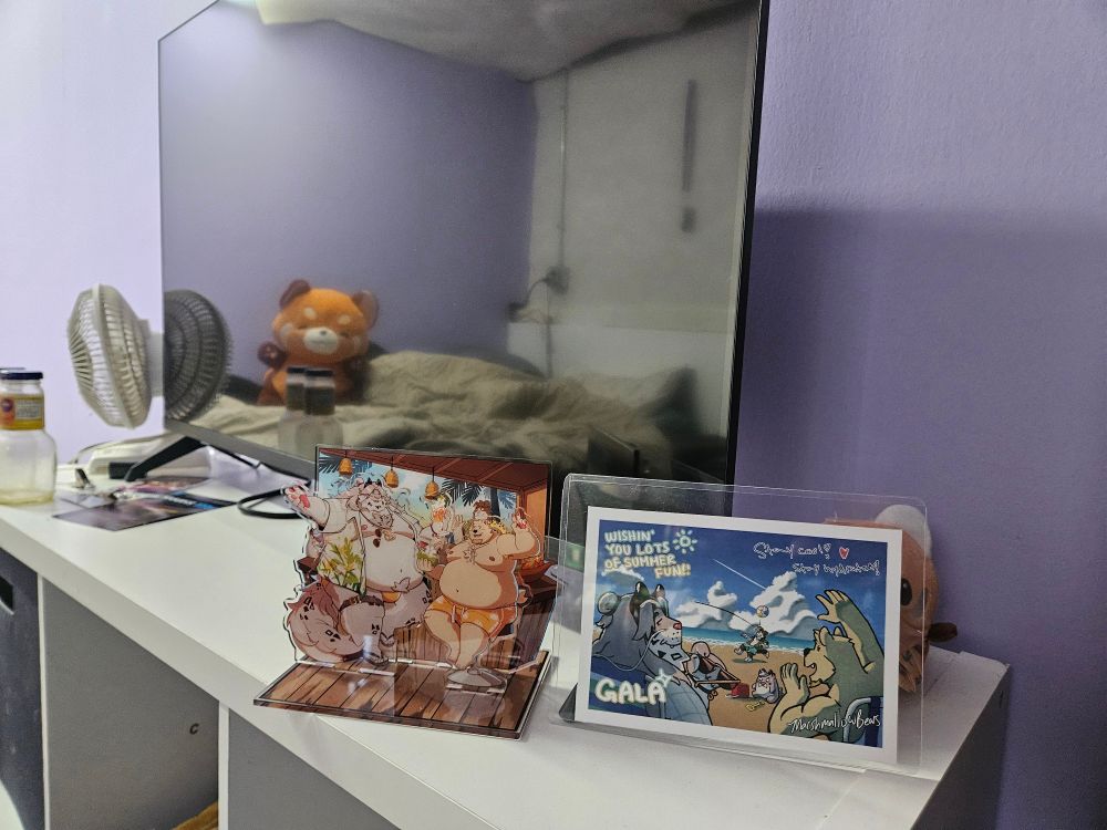 Acrylic standee and a postcard showing a fat kermode bear sharing a drink with a big dragon cat. 