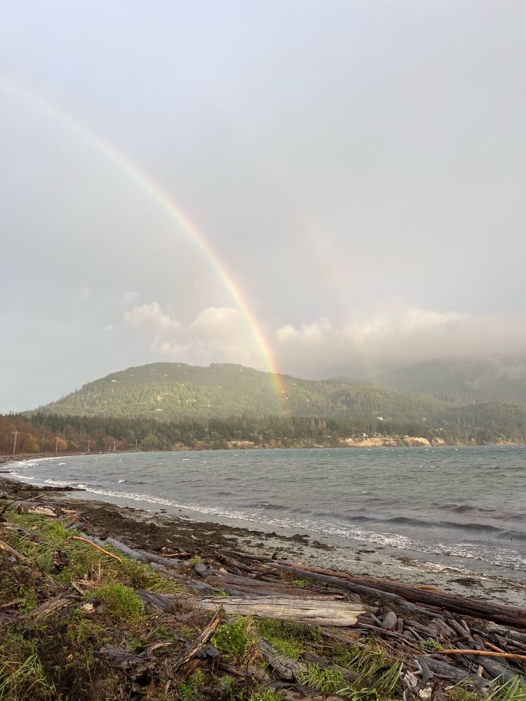 Rainbow over a beach with forested mountain behind.