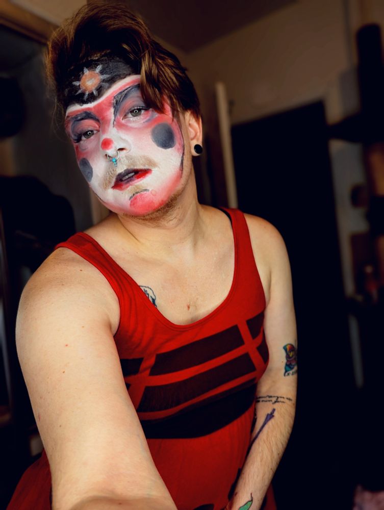 Fox has his face painted to look like a dalek with black cheeks and red shading around his eyes cheeks nose and chin. Above his eyebrows is backed out with a dalek eyestalk painted. He is also wearing a red Dalek dress