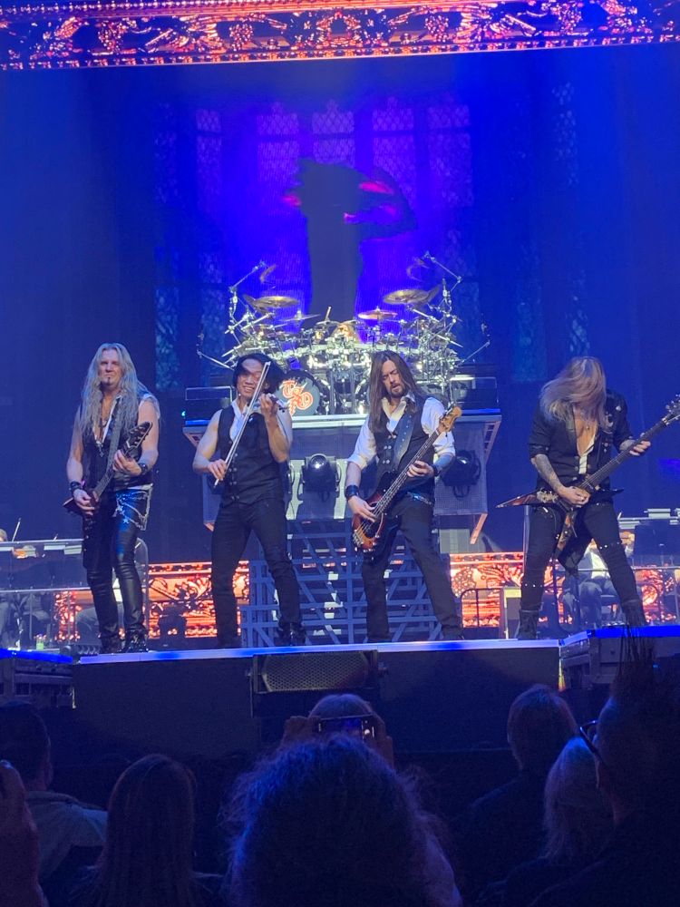 TSO members: guitar, electric violin, bass, guitar with drums in back 
