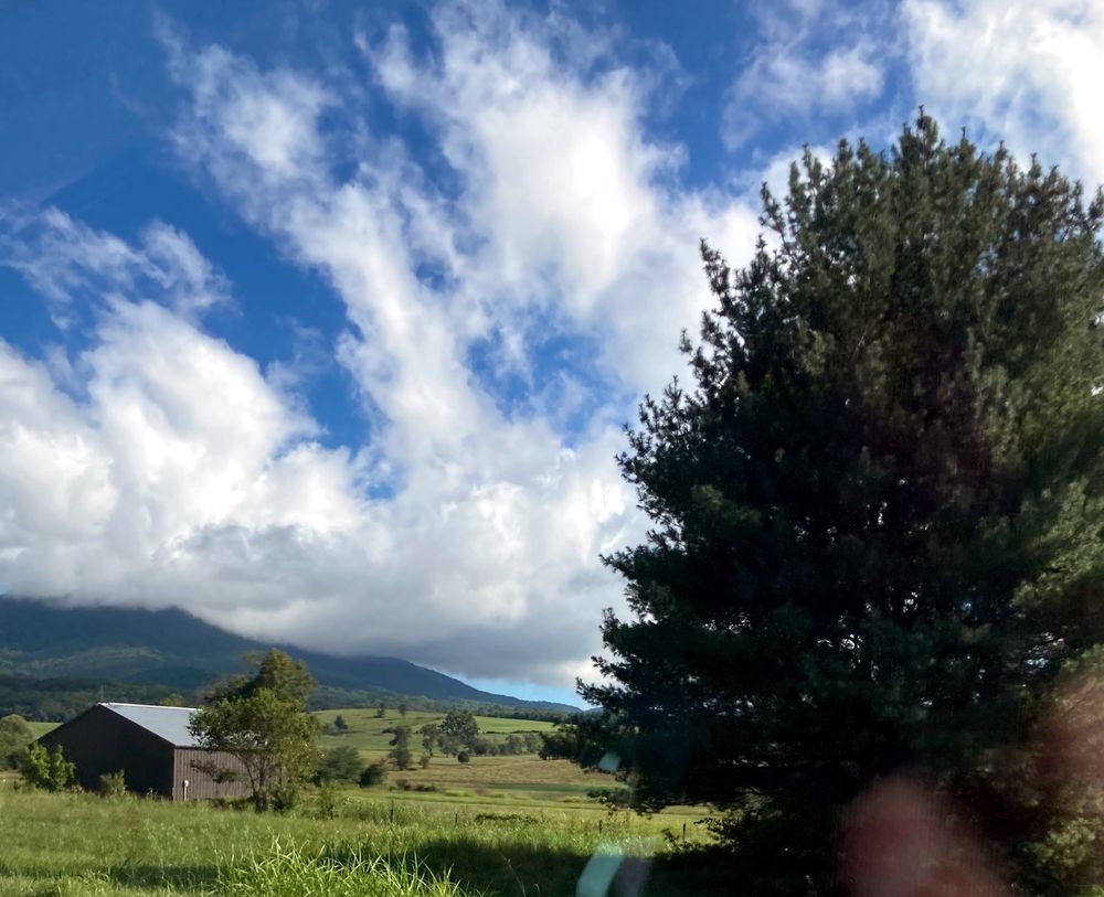 photo of a farmhouse w a large tree in the foreground. the sky is being magnificent again 