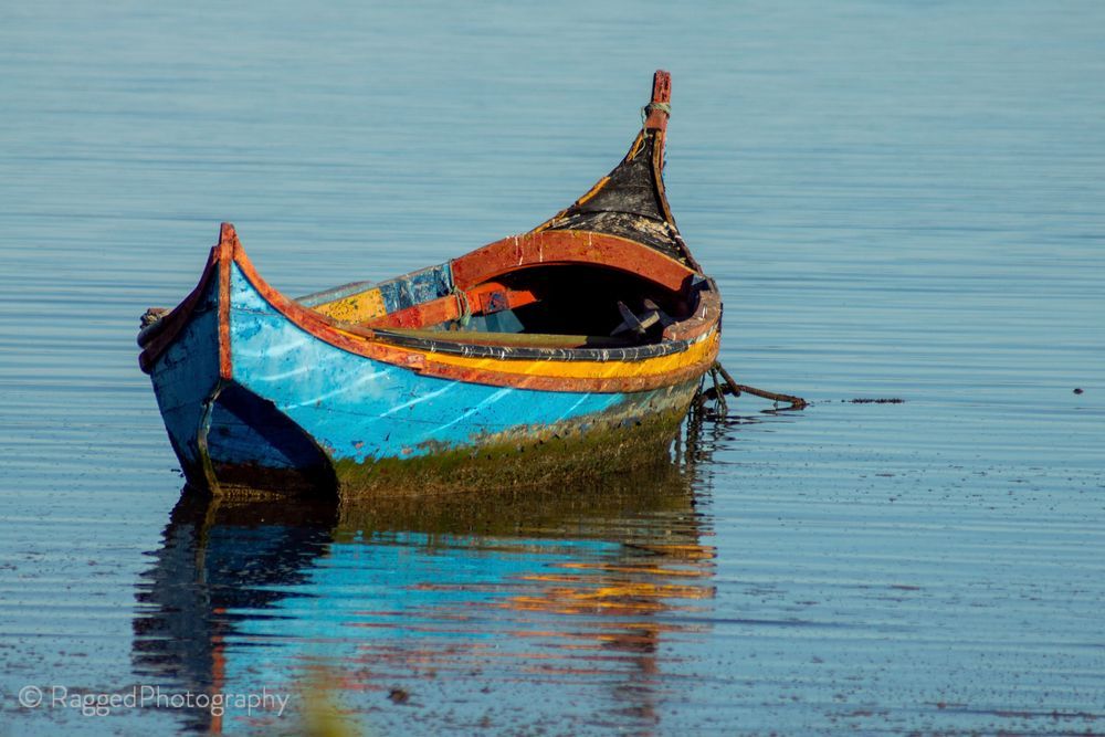 A small blue and orange rowing boat floating on a calm sea.
