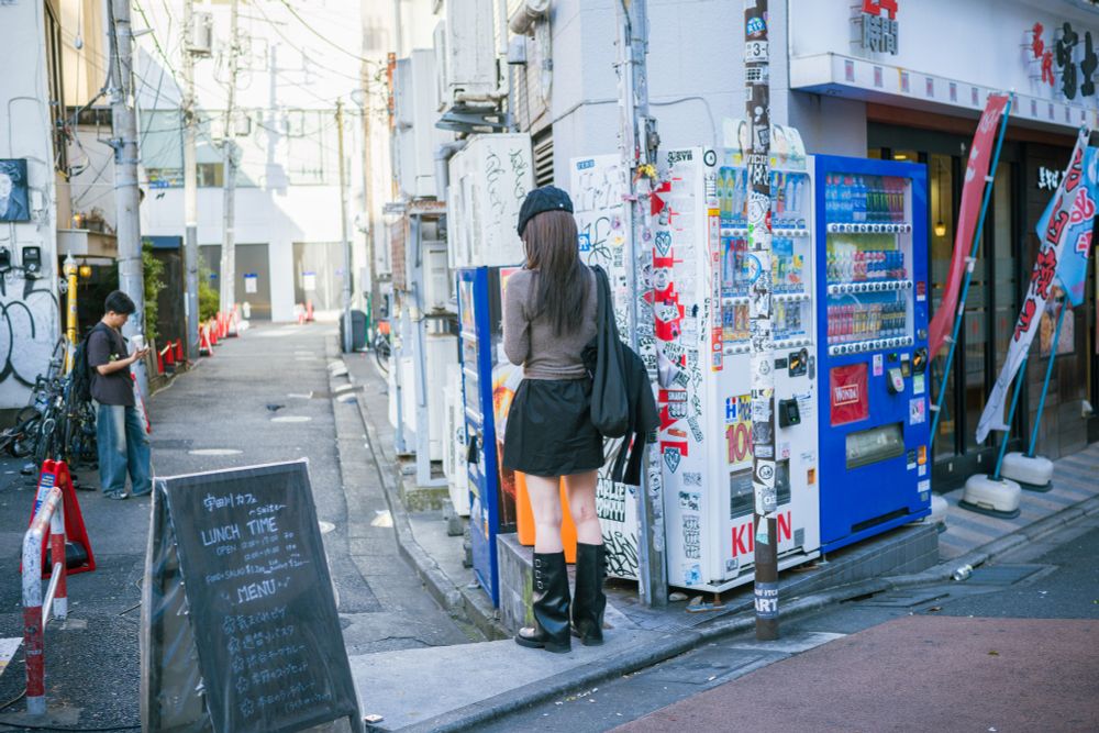 渋谷の人々　日本人女性１名　お洒落なカフェの看板の横でスマホを見つめる女性