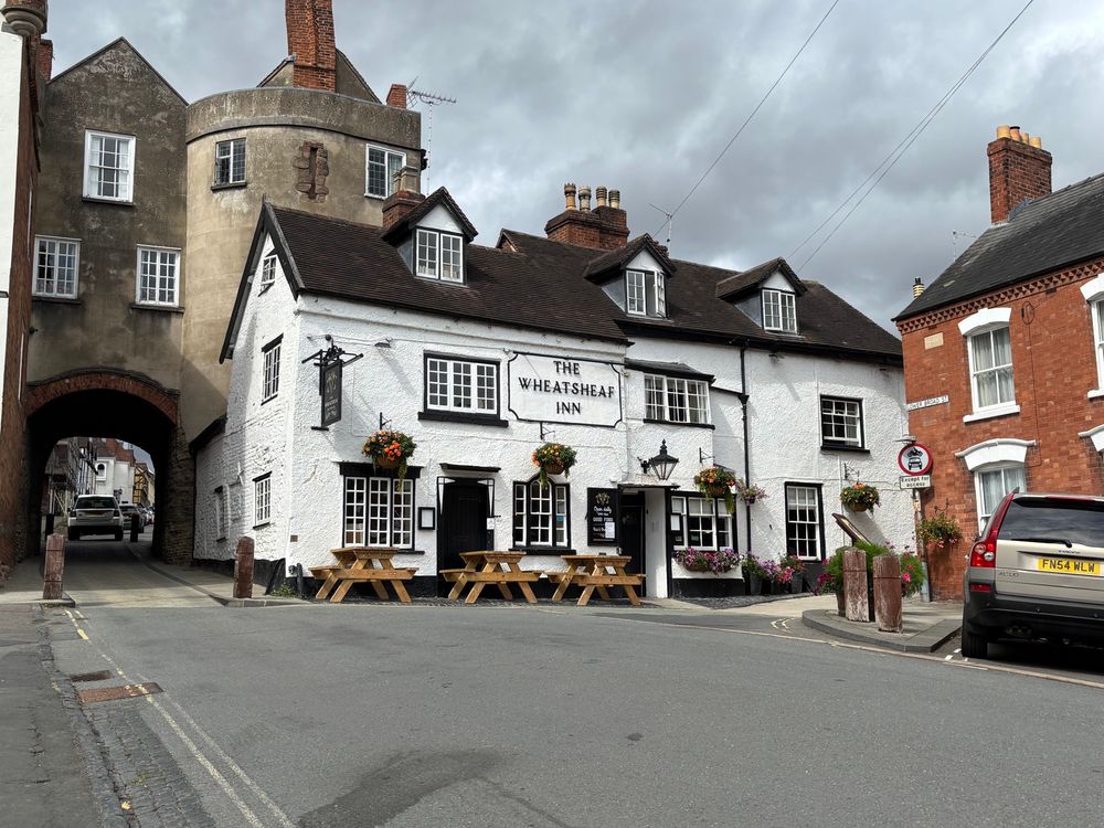 Photo of an old pub called the Wheatsheaf. Painted white with wooden tables outside. 