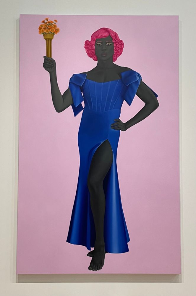 Amy Sherald’s painting Trans Forming Liberty, who is a gorgeous Black trans woman in a satin-y blue dress with a slit all the way up her thigh. She has pink hair & is holding a torch of yellow & orange flowers. 