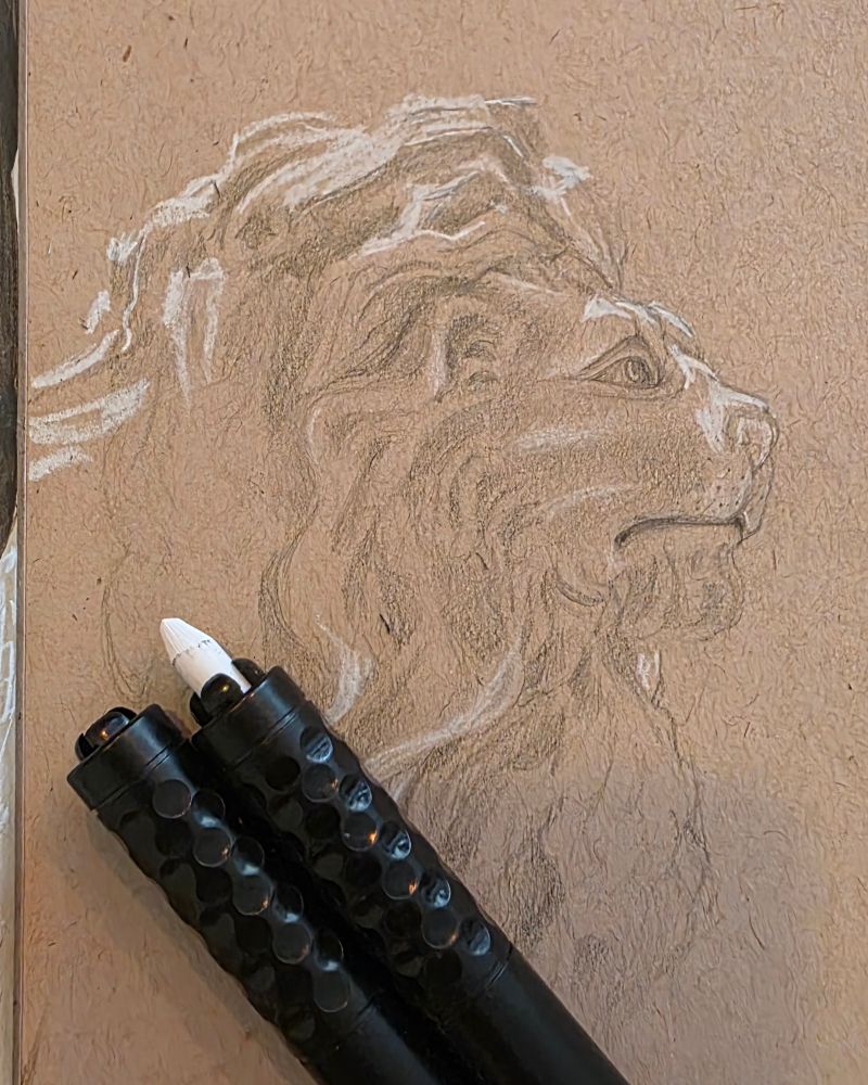 Photo of a mid toned brown paper sketchbook. In pencil and white chalk, a rough sketch of a crude garden sculpture of a lion lit from above. On the paper are two lead holders, one of white holds white chalk