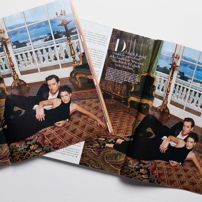 A photo of two copies of Harper's Bazaar Magazine, depicting Gavin Newsom and his then-wife Kimberly Guilfoyle, in a suit and halterneck black gown with heels respectively, sprawled langyidly together for the camera on a vintage rug in an opulent room with gold towering candlesticks, velvet and gilt armchair, in front of massive glass double doors revealing a classical white stone balcony overlooking a multi-million dollar view of the San Francisco Bay. 