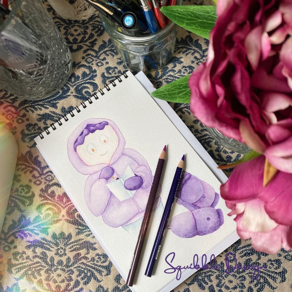 My sketchbook on my desk with two coloured pencils displaying illustrations of my character and a pair of mittens.
