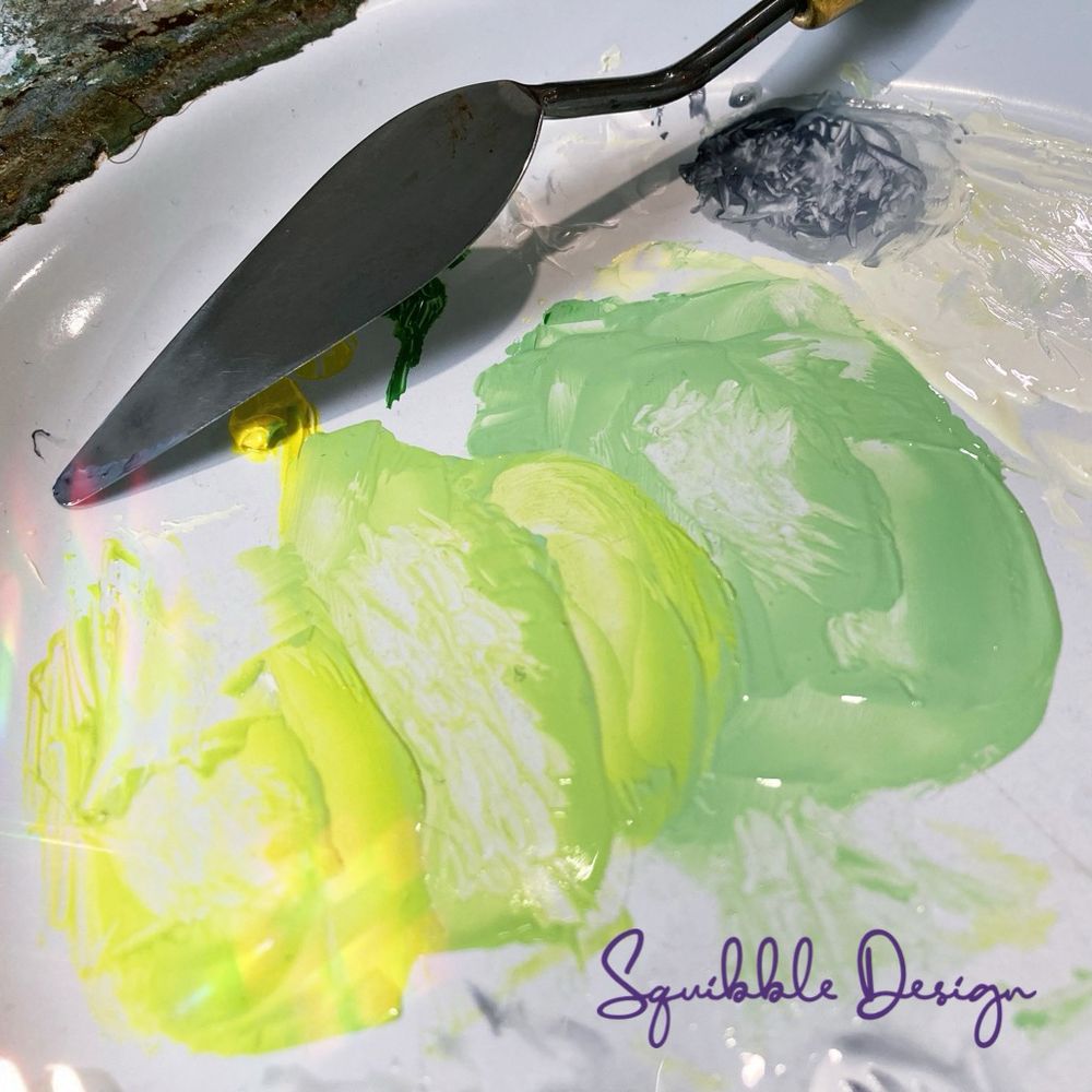 A series of pretty pale green paint swatches on my palette making up a lovely gradient! My palette knife is next to the swatches.