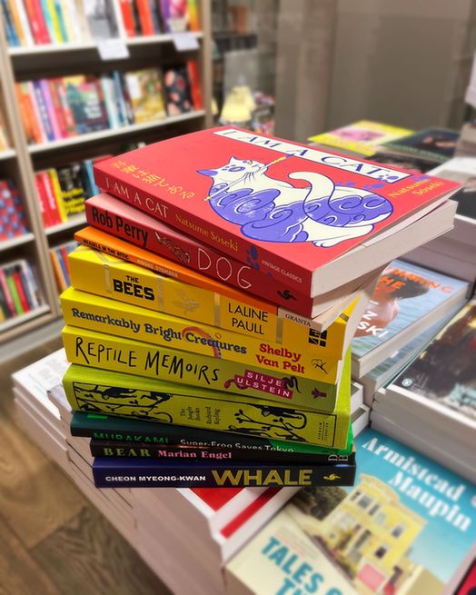 A stack of books, arranged by colour, photographed in a bookshop. Each book is inspired by an animal. Books featured include: Dog by Rob Perry, The Bees by Laline Paull, Bear by Marian Engel, Super-Frog Saves Tokyo by Haruki Murakami,
Whale by Cheon Myeong-kwan and more.