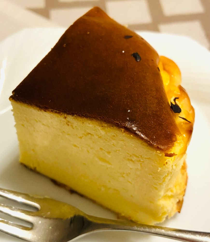 ワンホールの1/4にカットされたチーズケーキ。断面は滑らかで明るいベージュ色。焼き目は濃いめの焦茶でツヤっとしている、